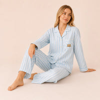Pyjama 100 coton femme rayé bleu porté par une femme assise au sol, coupe ample et ourson sur la poche